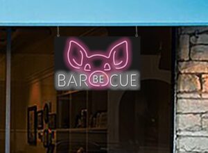 Illuminate your outdoor space with this unique Barbecue with Pig Face Graphic Neon Sign, featuring white letters and pink pig design on a large 32" x 20" sign. Perfect for backyard gatherings.